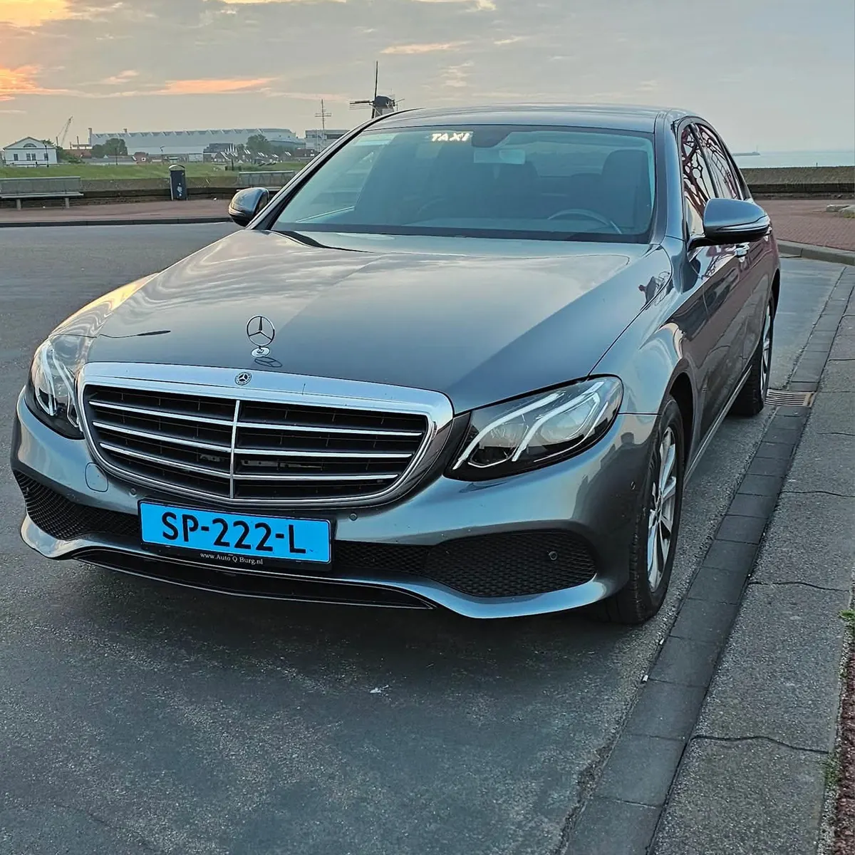 Taxi Cozy Mercedes E-Class aan de kust van Vlissingen, met een molen op de achtergrond